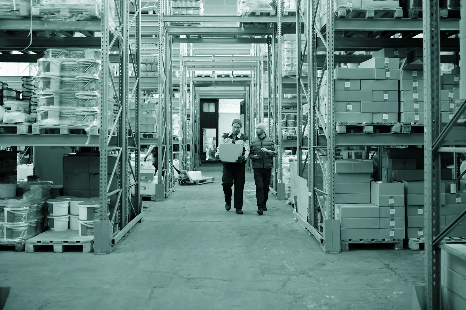 Two workers handle a package in a spacious warehouse surrounded by shelves stocked with boxes and products.