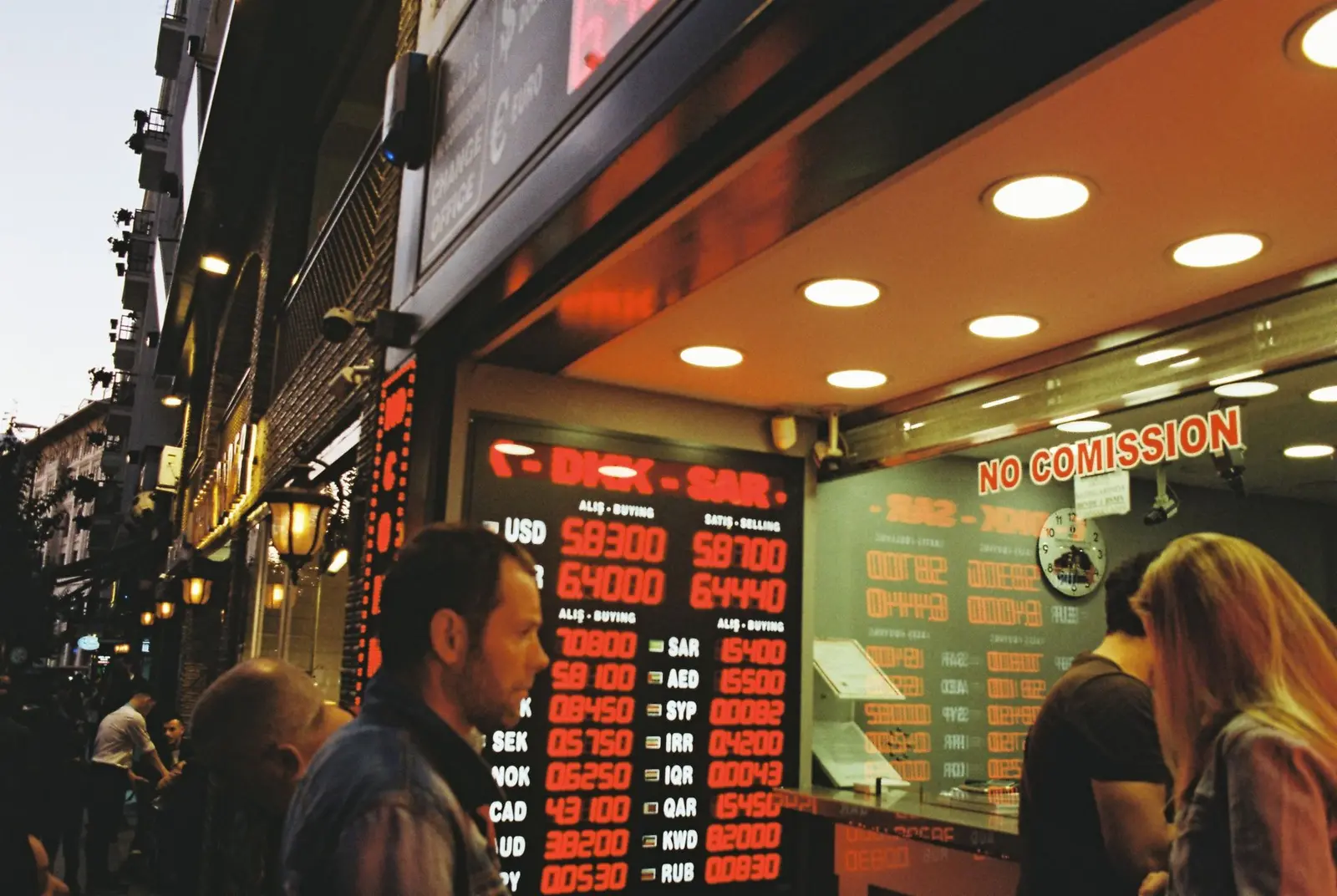 People gathering at a currency exchange office on a busy city street during dusk.