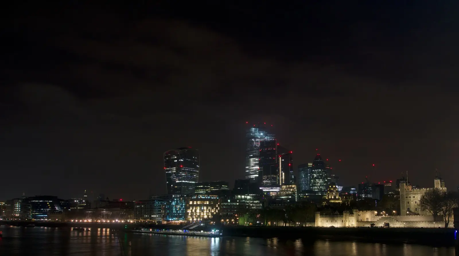 Dramatic night view of London's skyline featuring modern skyscrapers and the historical Tower of London.