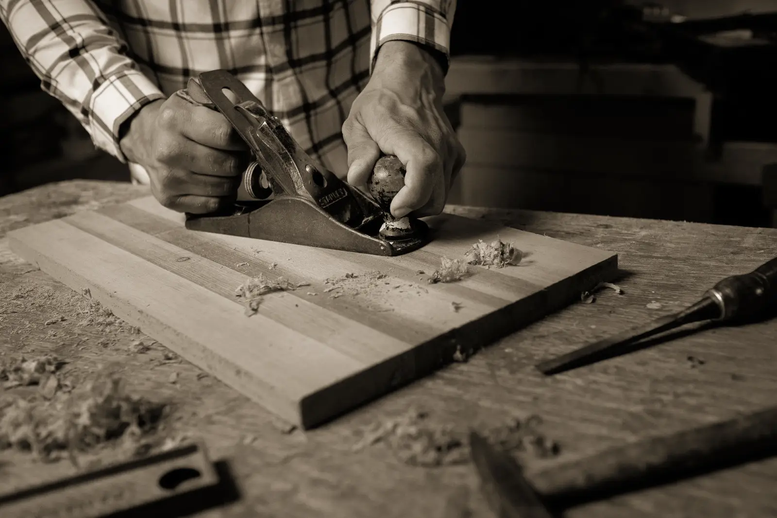 Close-up of a craftsman using a wood planer on a workbench. Hands engaged in precise woodworking craft.