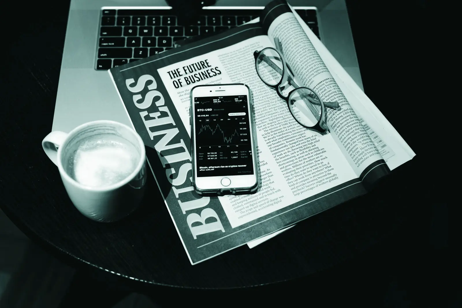A business setup with a laptop, coffee, phone, and newspaper. Perfect for finance themes.